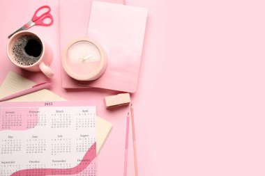 Takvimle kompozisyon, bir fincan kahve, çalar saat ve pembe arka planda durağan.
