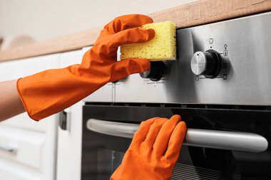 Turuncu lastik eldivenli kadın elektrikli fırını süngerle temizliyor.