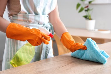 Turuncu lastik eldivenli kadın ahşap tezgahı bez ve deterjanla temizliyor.