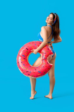 Mavi arka planda donut şeklinde yüzme yüzüğü olan genç bir kadın.