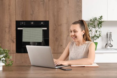 Mutfaktaki masada dizüstü bilgisayarla çalışan serbest çalışan bir kadın.