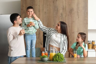 Mutlu ebeveynler ve küçük çocukları mutfakta portakal suyu içiyorlar.