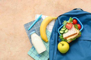 Sırt çantası, kırtasiye malzemesi ve turuncu arka planda lezzetli yemekler.