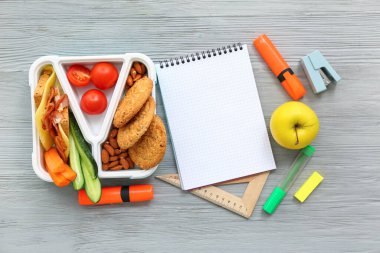 Boş defter, kırtasiye ve beslenme çantası. Gri ahşap arka planda lezzetli yemekler.