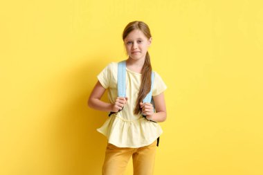 Sarı arka planda sırt çantalı küçük kız.