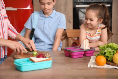 Anne, küçük çocuklarına mutfakta öğle yemeği hazırlıyor.