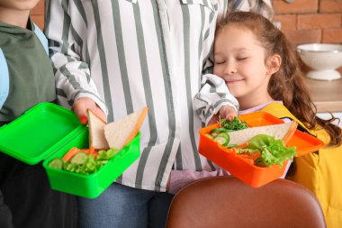 Okulda öğle yemeği yiyen küçük çocuklar ve mutfakta anneleri, yakın çekim.