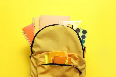 Not defterleri, suluboya boyalar ve sarı arkaplanda işaretler olan okul çantası