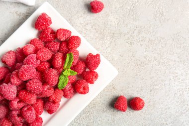 Taze ahududu tabağı ve gri arka planda nane şekeri.