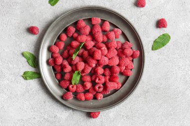 Taze ahududu tabağı ve gri arka planda nane şekeri.
