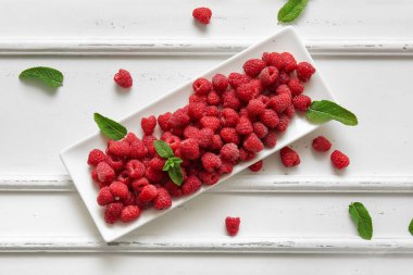 Taze ahududu tabağı ve beyaz arka planda nane şekeri.