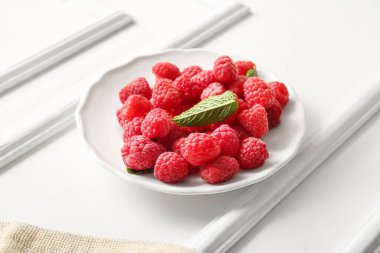 Taze ahududu tabağı ve beyaz arka planda nane şekeri.