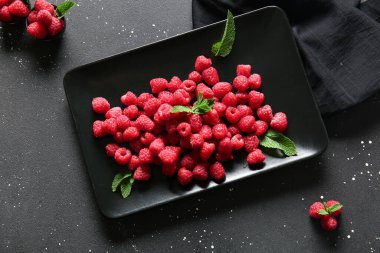 Siyah arka planda taze ahududu tabağı ve kâseleri.