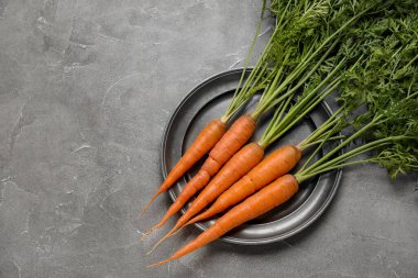 Gri arka planda yaprakları olan taze havuç tabağı.