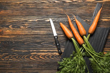 Tahta arka planda yaprakları olan taze havuçlar.