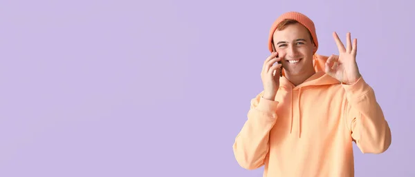 Młody Człowiek Telefonem Komórkowym Pokazuje Gest Liliowym Tle Miejscem Tekst — Zdjęcie stockowe