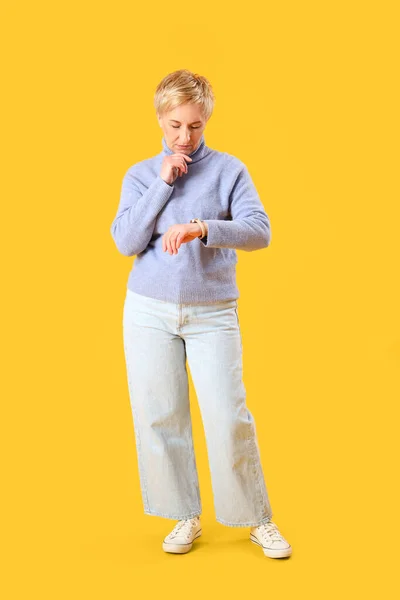 Thoughtful Mature Woman Looking Wristwatch Yellow Background — Stock Photo, Image