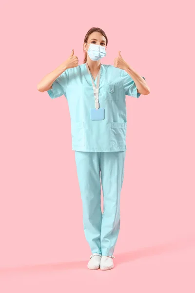 Žena Lékařská Stážistka Masce Ukazující Palce Nahoru Růžovém Pozadí — Stock fotografie