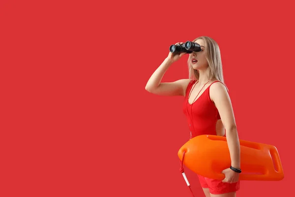Female lifeguard with binoculars and rescue buoy on red background