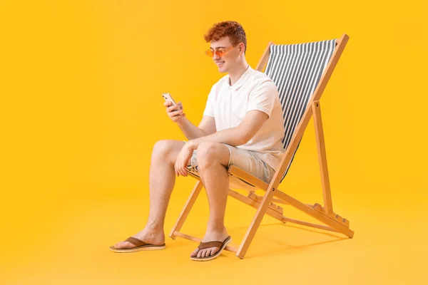 Mladý Muž Pomocí Mobilního Telefonu Palubě Židle Žlutém Pozadí — Stock fotografie