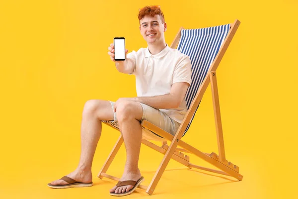 Mladý Muž Mobilním Telefonem Odpočívá Lehátku Žlutém Pozadí — Stock fotografie