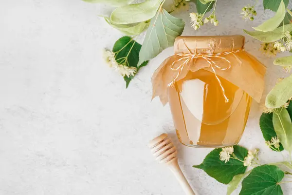 薄い背景にリンデン蜂蜜とディッパー付きガラス瓶 — ストック写真