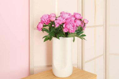 Raflarda pembe şakayık vazosu. Giyinme ekranı renk duvarının yanında.