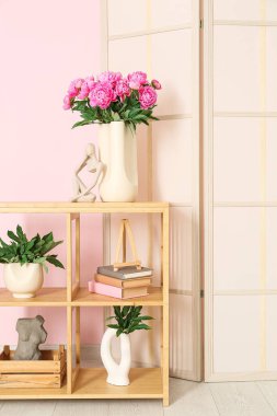 Rafların üzerinde pembe şakayık ve biblo vazosu ve renk duvarına yakın giyinme ekranı var.