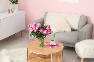 Kahve masasında pembe şakayık vazosu ve oturma odasında kanepe.