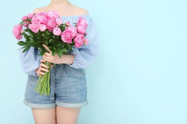 Mavi arka planda pembe şakayık buketi tutan kadın.