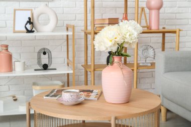 Beyaz şakayık vazosu sehpanın üzerinde, kanepe ve raf ünitesi beyaz tuğla duvarın yanında.