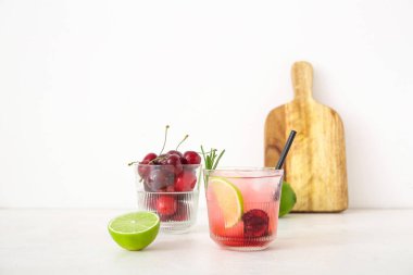 Bir bardak limonlu vişneli limonata ve beyaz arka planda biberiye.