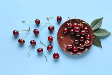 Tatlı kirazlı tabak ve mavi arka planda yapraklar.