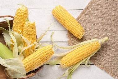 Beyaz ahşap arka planda taze mısır koçanları olan sepet.