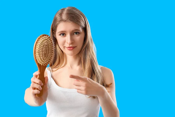青の背景にブラシを指して脱毛の問題を持つ若い女性 — ストック写真