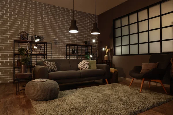 Interior of dark living room with cozy grey sofa and glowing lamps