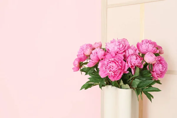 Vase of pink peonies with dressing screen near color wall