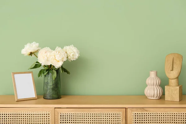 緑の壁の近くのドレッサーに写真フレームとフィギュアと白い牡丹の花瓶 — ストック写真