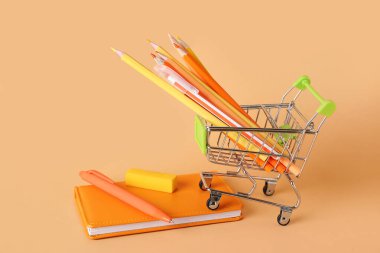 Renk arkaplanında farklı kırtasiye malzemesi olan alışveriş arabası