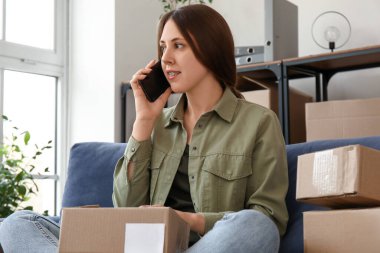Evde paketli genç bir kadın cep telefonuyla konuşuyor.