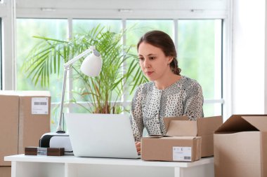 Ofiste dizüstü bilgisayar kullanan paketli genç bir kadın.