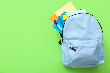 Yeşil arka planda not defterleri ve işaretleri olan mavi okul çantası