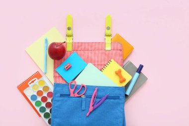 Mavi okul çantalı, defterli, suluboyalı ve pembe arkaplanlı bir elma.