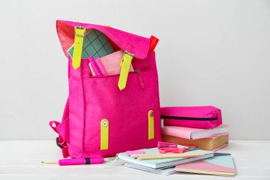 Kitaplarla dolu pembe okul çantası, kalem kutusu ve duvar kenarındaki beyaz ahşap masa üzerindeki kırtasiye malzemesi.