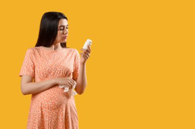 Sarı arka planda hapları olan hasta hamile kadın.