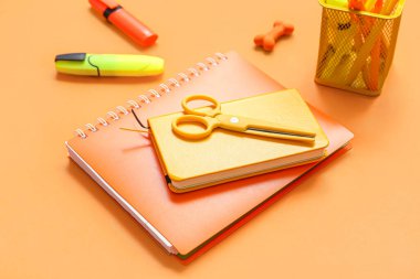 Turuncu arkaplanda farklı kırtasiye malzemesi olan defterler, yakın plan