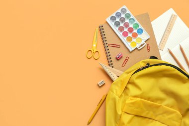 Turuncu arka planda boya ve kırtasiye malzemesi olan okul çantası.