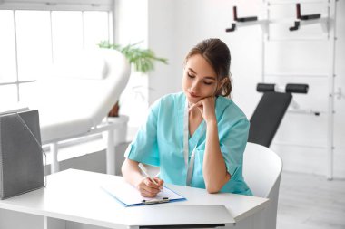 Kadın stajyer doktor hastanede panoya yazı yazıyor.