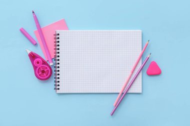 Mavi arkaplanda farklı kırtasiye malzemesi olan boş bir defter