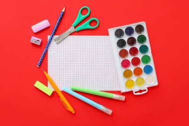 Kırmızı zemin üzerinde farklı kırtasiye malzemesi olan boş bir defter